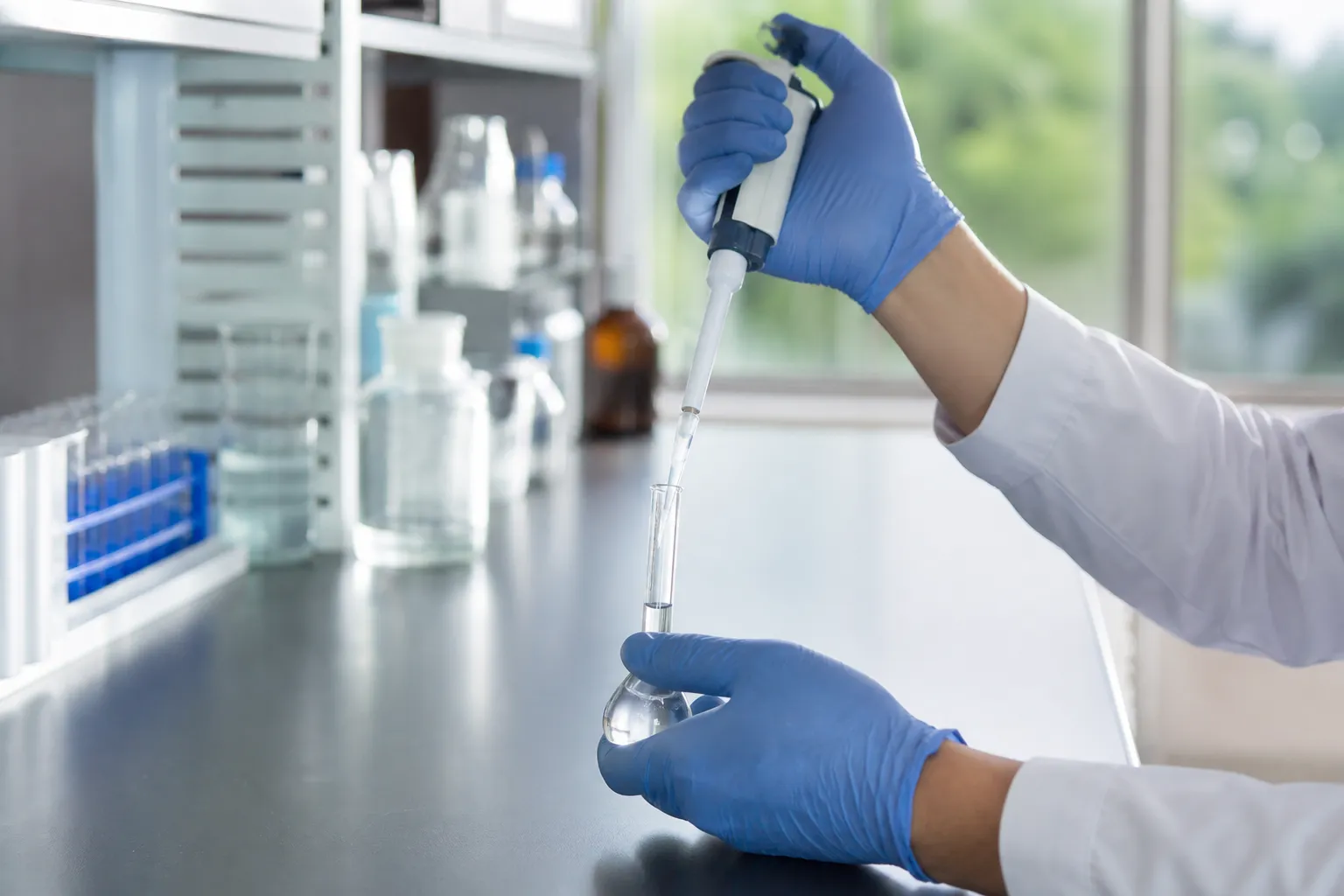 Laboratory technician using a micropipette with a small volumetric flask